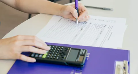 Person filling out a budget sheet with a calculator